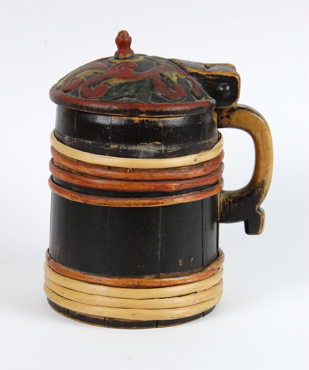 Kanne av trestaver. Lokk med rødt, gult og grønt akantusskurd. Korpus med fire gjorder oppe og nede, fire av gjordene er av nyere dato, sotmalet. hanken er skåret ut av en stav.