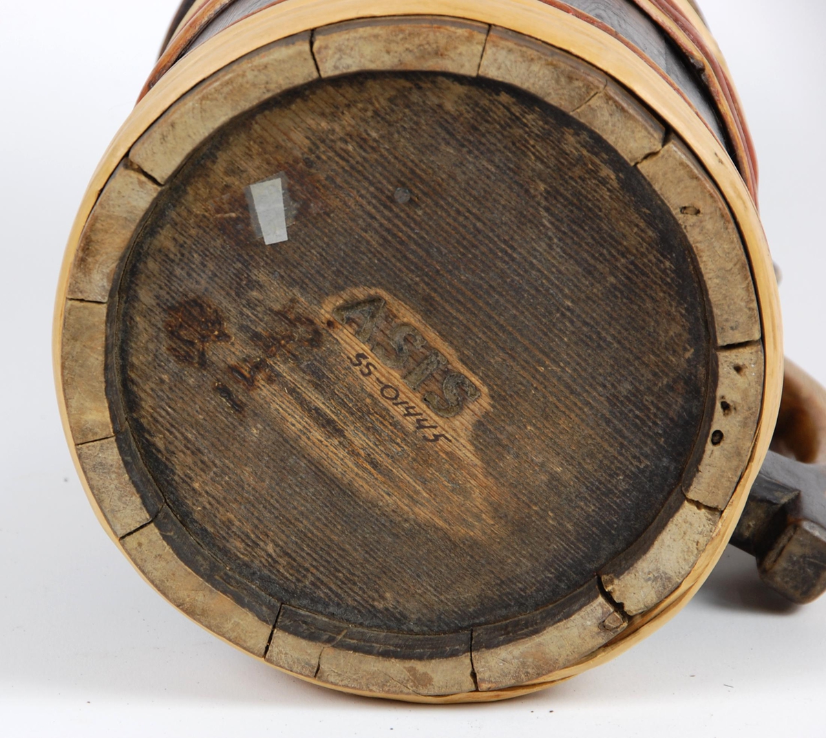 Kanne av trestaver. Lokk med rødt, gult og grønt akantusskurd. Korpus med fire gjorder oppe og nede, fire av gjordene er av nyere dato, sotmalet. hanken er skåret ut av en stav.