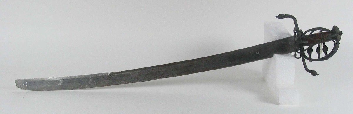 Pyramideformet knapp med kryssfilt dekor og asymmetrisk feste med 3 sidebøyler med fortykninger på midten på utsiden og en på innsiden. Nyreformet parerplate på utsiden og klingebrekker og tommelbøyle på innsiden. S-formede, runde parérstenger med fortykning med filt dekor og dråpeformet avslutning.
Tregrep. Enegget krum, kileformet klinge med en ryggstillt blodrand. Ryggslipt mot spissen. Spiss brukket. Tre hull på spiss. Ett smedstempel.

