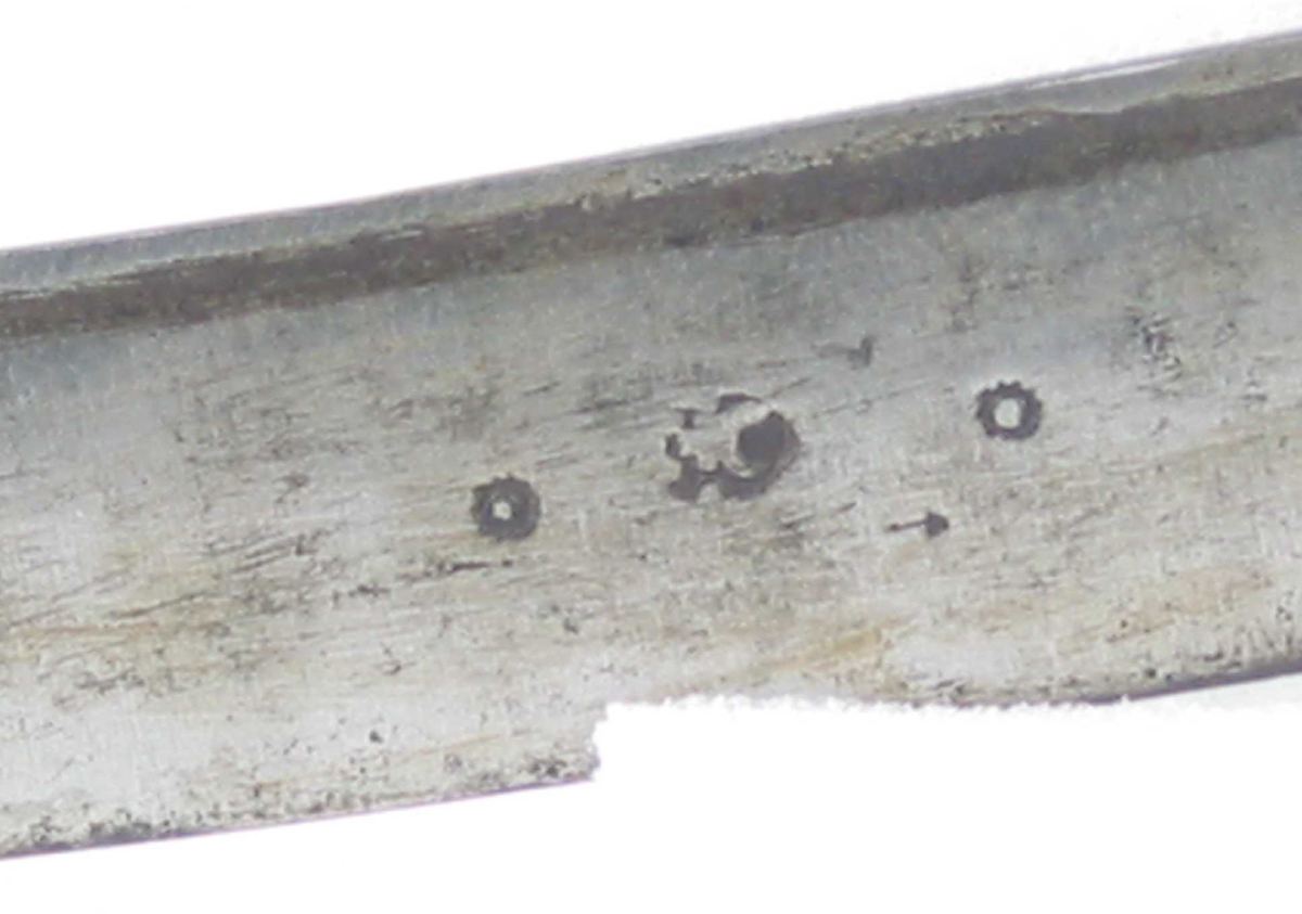 Pyramideformet knapp med strekdekor. Asymmetrisk kurvfeste med to sidebøyler( øverste avbrukket )med riflede fortykkelser på midten. mellom håndbøylen og kurvens ytterkant. Innsiden har en  sidebøyle. Kurvens basis er på utsiden en kvadratisk parérplate med to hjerteformede gjennombrytninger. På innsiden er det en klingebrekker og tommelbøyle. Opp og nedbøyde parérstenger med riflede fortykkelser på endene.
Tregrep med nyere jerntrådvikling.
Enegget krum klinge med 3 hull ipå klingspissen og en smal hulslipning på ryggsiden.Tre smedmerker på venstre side. 