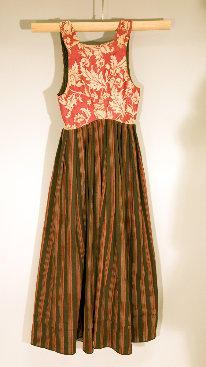 Håndsydd livkjole med stripete ullskjørt og rødt ullliv med store plantemotiv. Livet har rett hals bak, skjøtte seler og mangler ryggsøm. Lukningen består av fire par hekter og tre par hemper til snøring. Åpen klaff.
Fõr av stripete håndvevd ullstoff.
Nederst på skjørtet et børstebånd og skoning av et grindvevd bånd.
Skjørtet har en hengefald.