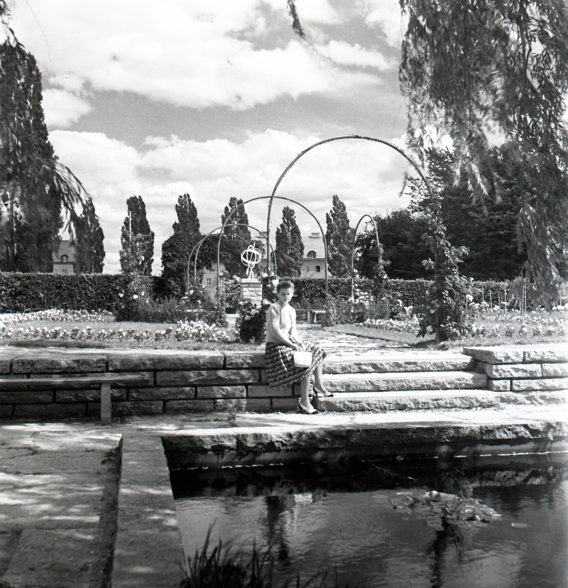 Einar Jagerwalls första bok, sid. 68: En idyll vid läroverket med rosengången, näckrosdamm och springbrunnen./ Parken vid Läroverket. Fru Mary Jagerwall sittande på stenmuren.