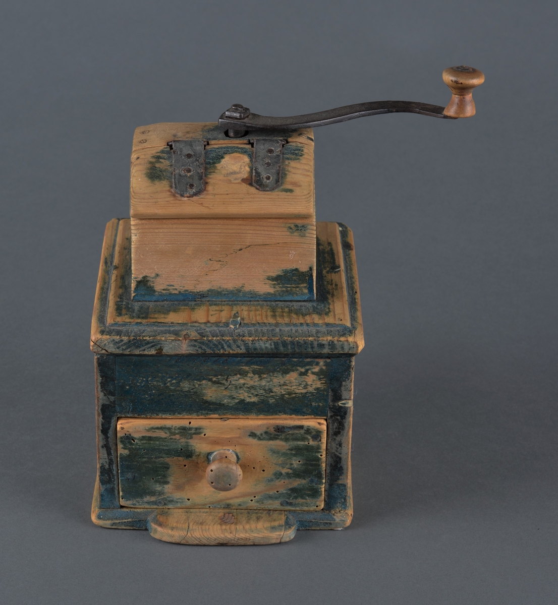 Kaffekvern i tre med kvadratisk bunn. Øverst et kaffehus med luke og innvendig kvern som dreies med en utvendig sveiv. Kvern og sveiv er i jern med en trekule til håndtak. Luka er hengslet til huset med streng. Nederst en utrekkbar skuff med trehåndtak. Kverna ser ut til å ha vært grønnmalt, men malinga er svært avslitt.