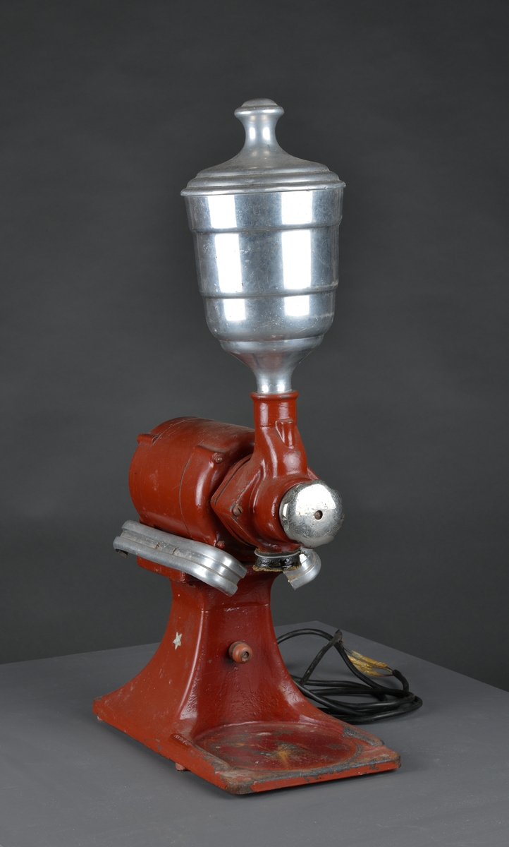 Motorisert kaffekvern som har stått i en landhandler. 
Kaffebønner helles i maskinen og males til kaffe, fortrinnsvis for kok-kaffe.

Det følger med en løs beholder for å samle opp den malte kaffen.

Maskina er rødlakkert, er slitt med noe rust og rester av olje eller fett.