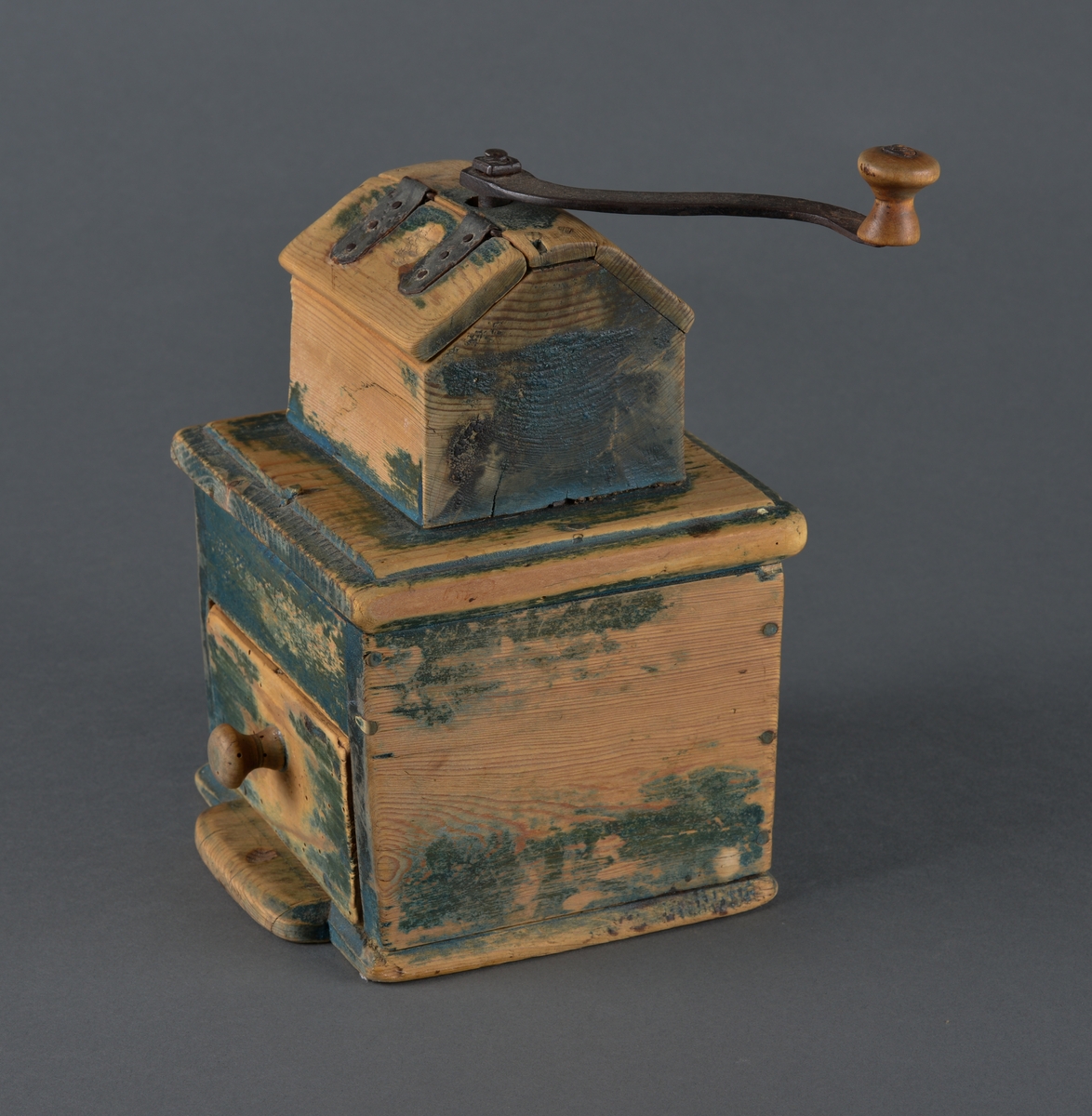 Kaffekvern i tre med kvadratisk bunn. Øverst et kaffehus med luke og innvendig kvern som dreies med en utvendig sveiv. Kvern og sveiv er i jern med en trekule til håndtak. Luka er hengslet til huset med streng. Nederst en utrekkbar skuff med trehåndtak. Kverna ser ut til å ha vært grønnmalt, men malinga er svært avslitt.