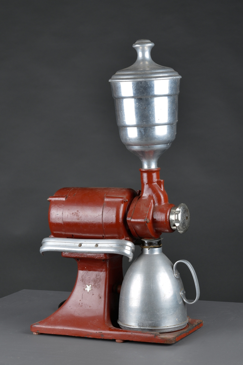 Motorisert kaffekvern som har stått i en landhandler. 
Kaffebønner helles i maskinen og males til kaffe, fortrinnsvis for kok-kaffe.

Det følger med en løs beholder for å samle opp den malte kaffen.

Maskina er rødlakkert, er slitt med noe rust og rester av olje eller fett.