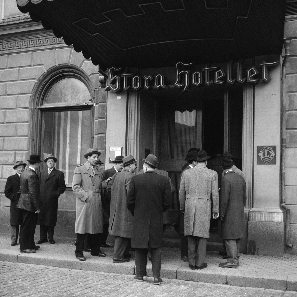 Serie bilder där fotografen följer en grupp herrar mot Stora hotellet i Linköping. Om vi tolkar fotoliggarens korta skrivelse rörde det sig om cykelhandlare som sammanförts av cykellyktstillverkaren Auto-Marin. 1957.