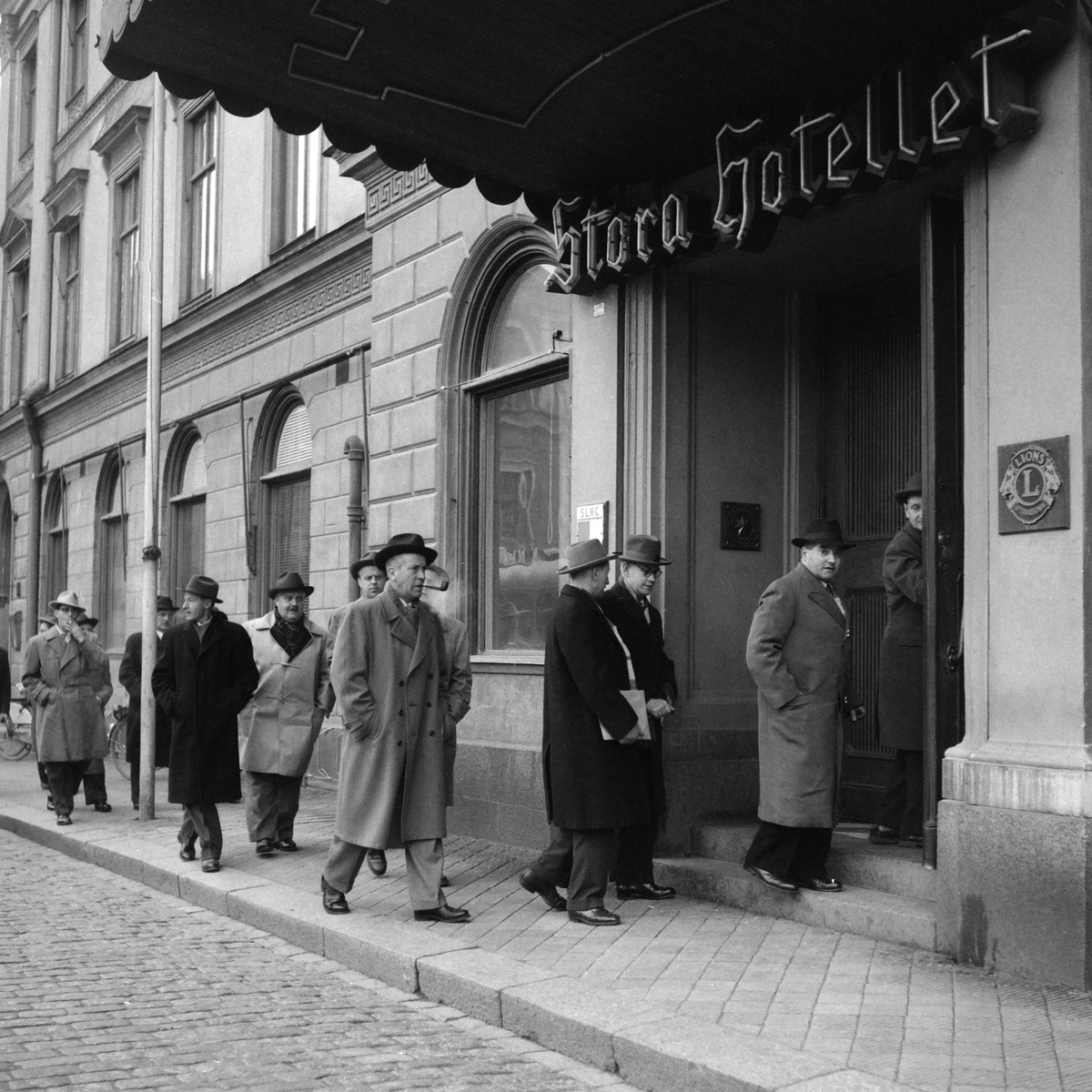 Serie bilder där fotografen följer en grupp herrar mot Stora hotellet i Linköping. Om vi tolkar fotoliggarens korta skrivelse rörde det sig om cykelhandlare som sammanförts av cykellyktstillverkaren Auto-Marin. 1957.