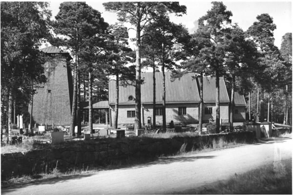 Exteriörbild av Rydöbruks kapell och kyrkogård. Kapellet återuppbyggdes 1957-1958 efter att kapellet från 1922 på platsen brann ner till grunden den 10 april 1957. Endast klockstapeln från 1925 klarade sig undan elden. Exteriören byggdes upp exakt som den gamla utifrån originalritningarna av Karl Martin Westerberg. För den nya interiören fanns redan ritningar, som upprättats 1954 inför en tilltänkt renovering.