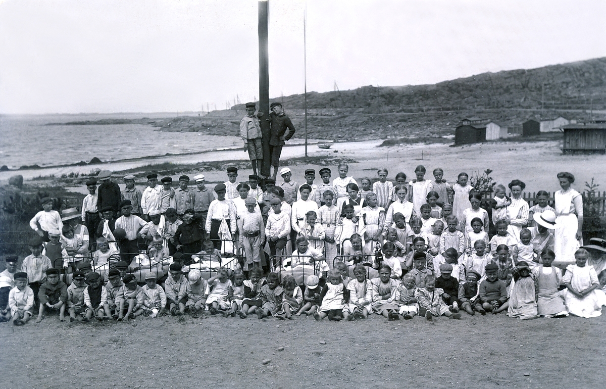 En stor samling skrofulösa (körteltuberkulos) barn som vårdades vid Kustsanatoriet Apelviken sommaren 1912. De minsta har burits ut med sängarna i det fria för att få sol, vilket var en del av behandlingen. Kanske är det samtliga som vistades där denna sommar. I bakgrunden syns stranden Lilla Apelviken med badhytter/bodar.