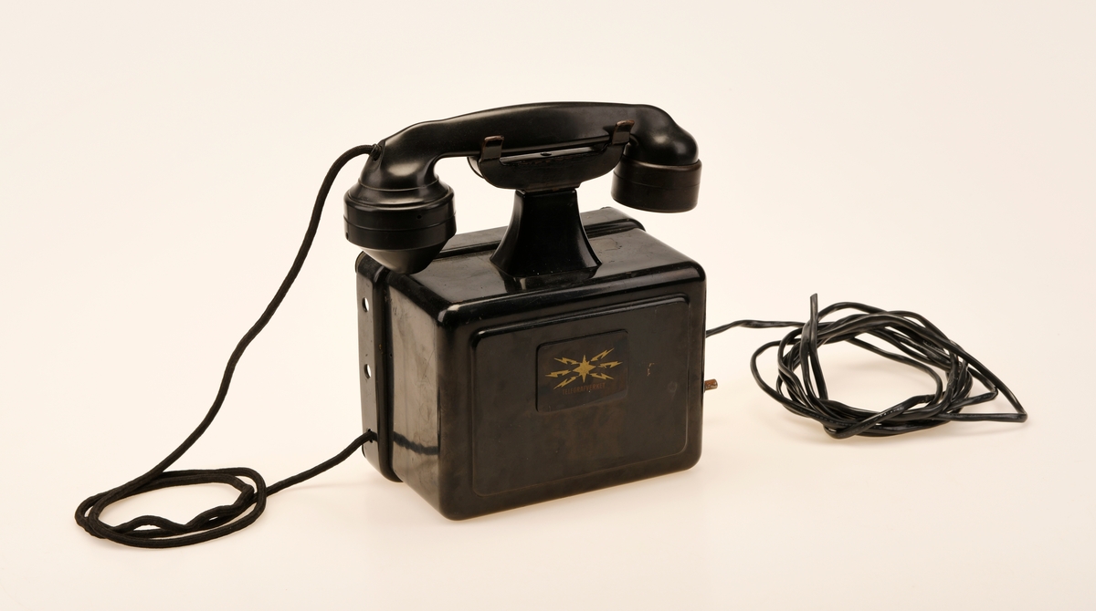 Sort bord/veggtelefon i Jernblikk og Bakelitt med sveivehåndtak. Telegrafverkets logo pryder fremsiden av aparatkassen. Ledningen som går fra aparatkassen til telefonrøret er av sort spiralisert tekstil. Telefonen har forøvrig en y-gaffel. Enden av ledningen som går til støpselet er kuttet av.