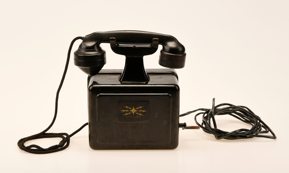 Sort bord/veggtelefon i Jernblikk og Bakelitt med sveivehåndtak. Telegrafverkets logo pryder fremsiden av aparatkassen. Ledningen som går fra aparatkassen til telefonrøret er av sort spiralisert tekstil. Telefonen har forøvrig en y-gaffel. Enden av ledningen som går til støpselet er kuttet av.