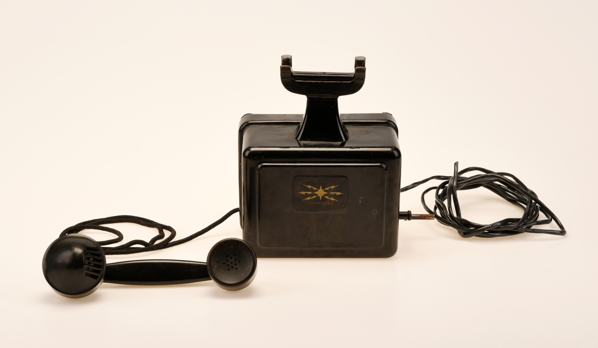 Sort bord/veggtelefon i Jernblikk og Bakelitt med sveivehåndtak. Telegrafverkets logo pryder fremsiden av aparatkassen. Ledningen som går fra aparatkassen til telefonrøret er av sort spiralisert tekstil. Telefonen har forøvrig en y-gaffel. Enden av ledningen som går til støpselet er kuttet av.