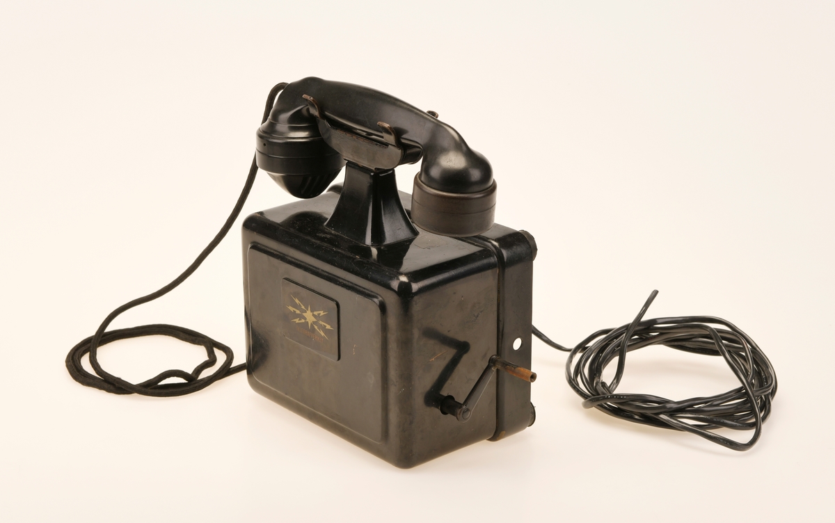 Sort bord/veggtelefon i Jernblikk og Bakelitt med sveivehåndtak. Telegrafverkets logo pryder fremsiden av aparatkassen. Ledningen som går fra aparatkassen til telefonrøret er av sort spiralisert tekstil. Telefonen har forøvrig en y-gaffel. Enden av ledningen som går til støpselet er kuttet av.