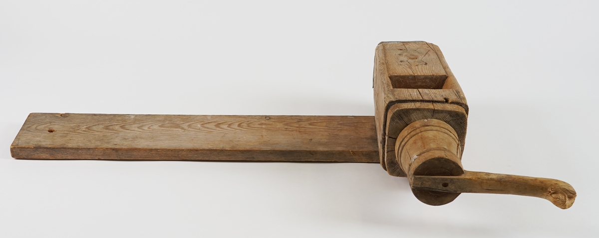 Potetkvern i tre. Består av eit trebrett/plank som underlag, ein sylinder med ei skrue inni, og ei sveiv.