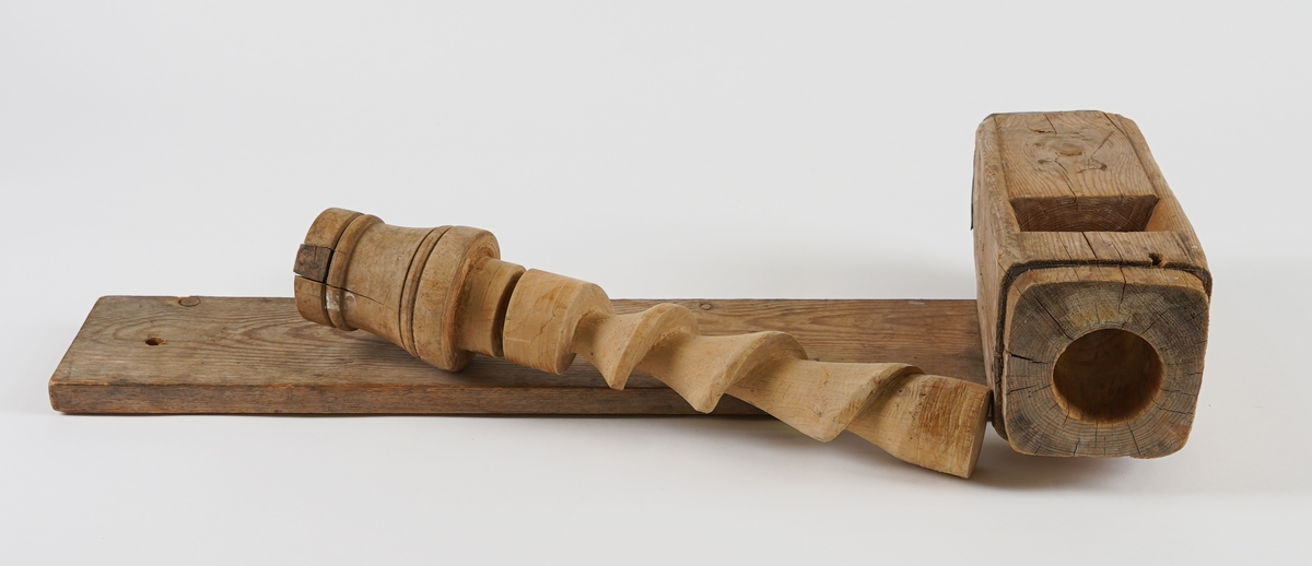 Potetkvern i tre. Består av eit trebrett/plank som underlag, ein sylinder med ei skrue inni, og ei sveiv.