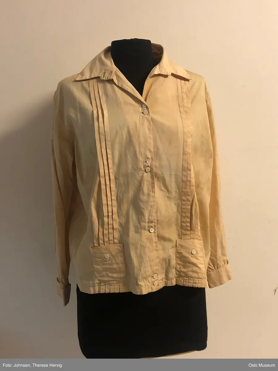 A: jakke med langer ermer, beige, lukkes med knapper i front. 
B: kjole, brudekjole med lange ermer. Løstsittende liv, langt skjørt med kort slep. Livet lukkes med trykknapper og hekter. Håndledd er er kantet med blonde. Påsydd belte med rosett på magen. 
C: slør stoff
D: blomsterkrans