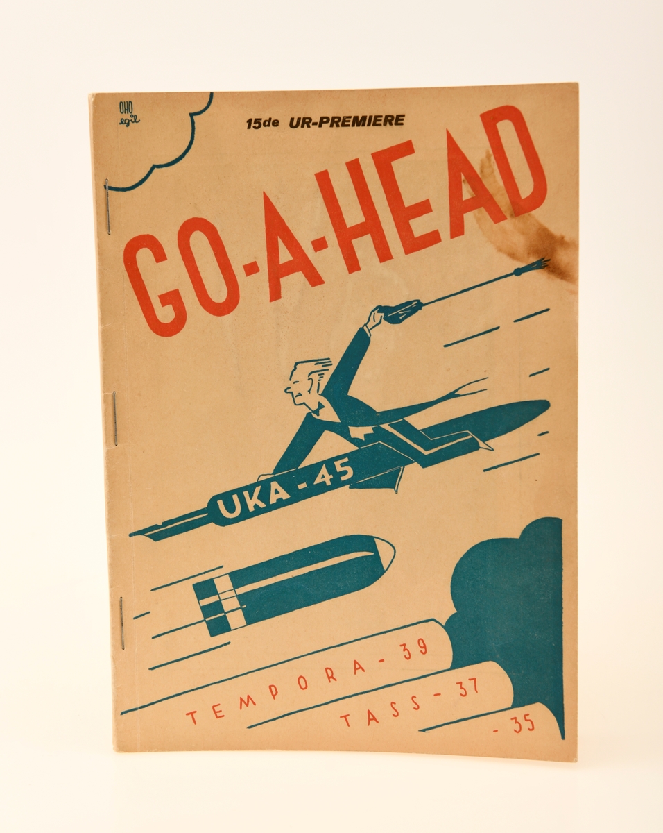 Programhefte for Go-a-head, UKA fra 1945. Dette heftet er identisk med standar heftet som ble utgitt, med unntak av skriften i sort øverst på forsiden: "15de UR-PREMIERE". Heftet inneholder selve programmet for UKA, en rekke sangtekster og reklamer fra diverse sponsorer. På forsiden ser vi en mann kledd i dress som rir en penn som om den skulle være en missil. Mannen holder fast i pennen med høyrehånden og en studentlue i sin venstre hånd. Øverst til venstre ser vi en liten sky som omgir en liten tekst. Under mannen ser vi artilleri som skyter i retningen den tidligere nevnte mannen kommer i fra. Nederst på forsiden ser vi noe som tilsynelatende er løpene til batterier. På disse står tekst som reffererer til navn til de 3 foregående UKA arrangementene nemlig: Tempora fra 1939, Vær-i-tass fra 1937, og Dek-e-du fra 1935. Heftet er på totalt 80 sider.