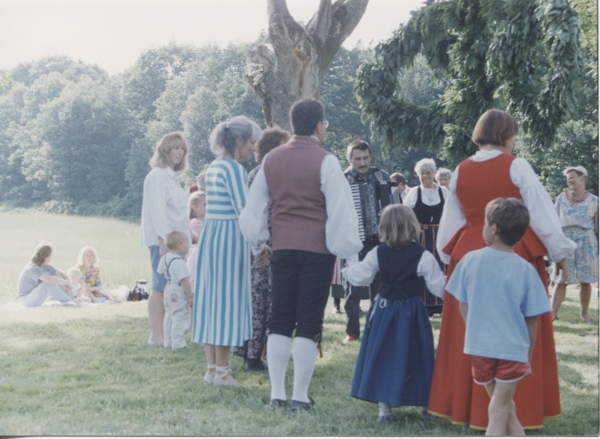 Midsommarfirande vid Hembygdsgården Långåker 1:3 1993. 
Med ryggen åt kameran står Staffan Bjerrhede klädd i folkdräkt. I röd folkdräkt står hans syster Annika Bjerrhede med sina barn Julia och Johannes Lundin. Övrigas namnuppgifter saknas.
Relaterade motiv: A03389 - A03408.