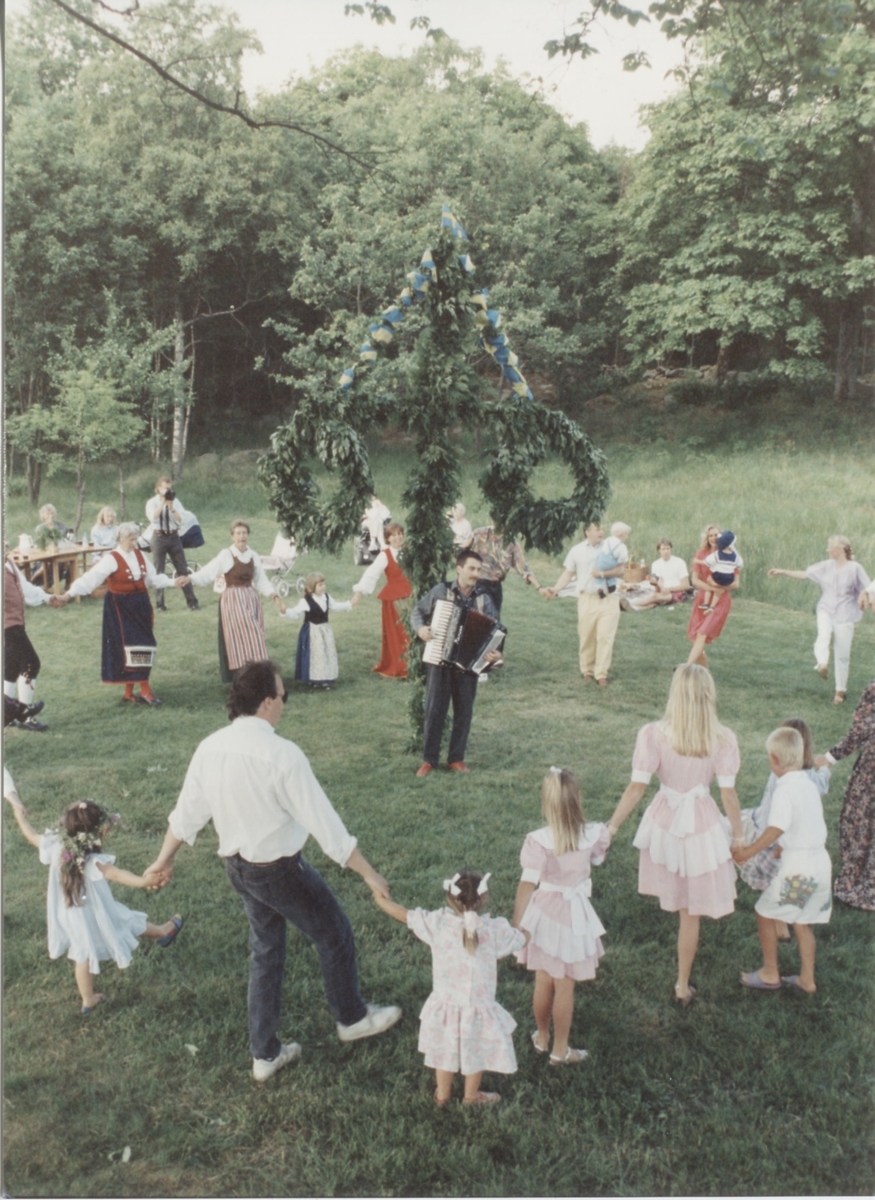 Midsommarfirande vid Hembygdsgården Långåker 1:3 1993. 
I folkdräkt med randigt förkläde dansar Karin Gustafsson. I röd folkdräkt Annika Bjerrhede (skymd bakom midsommarstången). Den manlige okände dragspelaren är från Göteborg, övriga namnuppgifter saknas.
Relaterade motiv: A03389 - A03408.