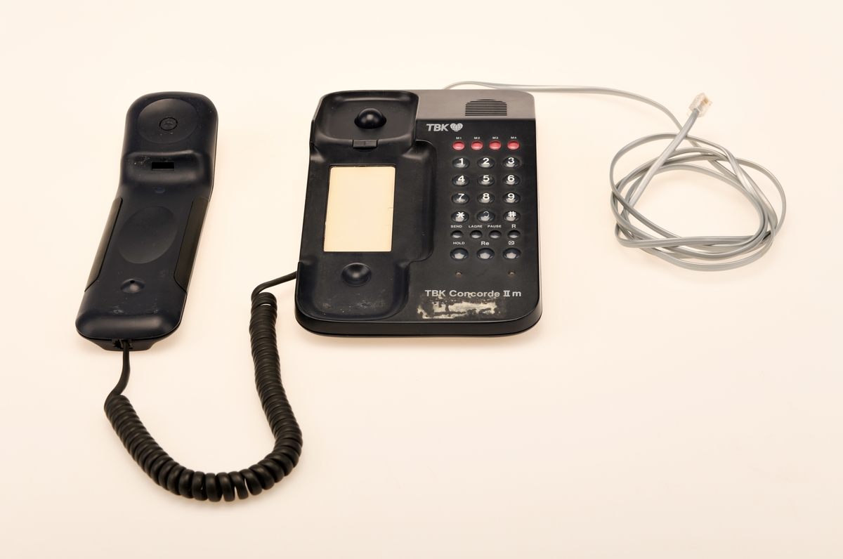 Sort bordtelefon med 23 taster fra TBK. Telefonen er av modelltypen TBK Concorde II m. Telefonen kommer med en svart spirallisert ledning til telefonrøret og en hurtigkopling i grått.