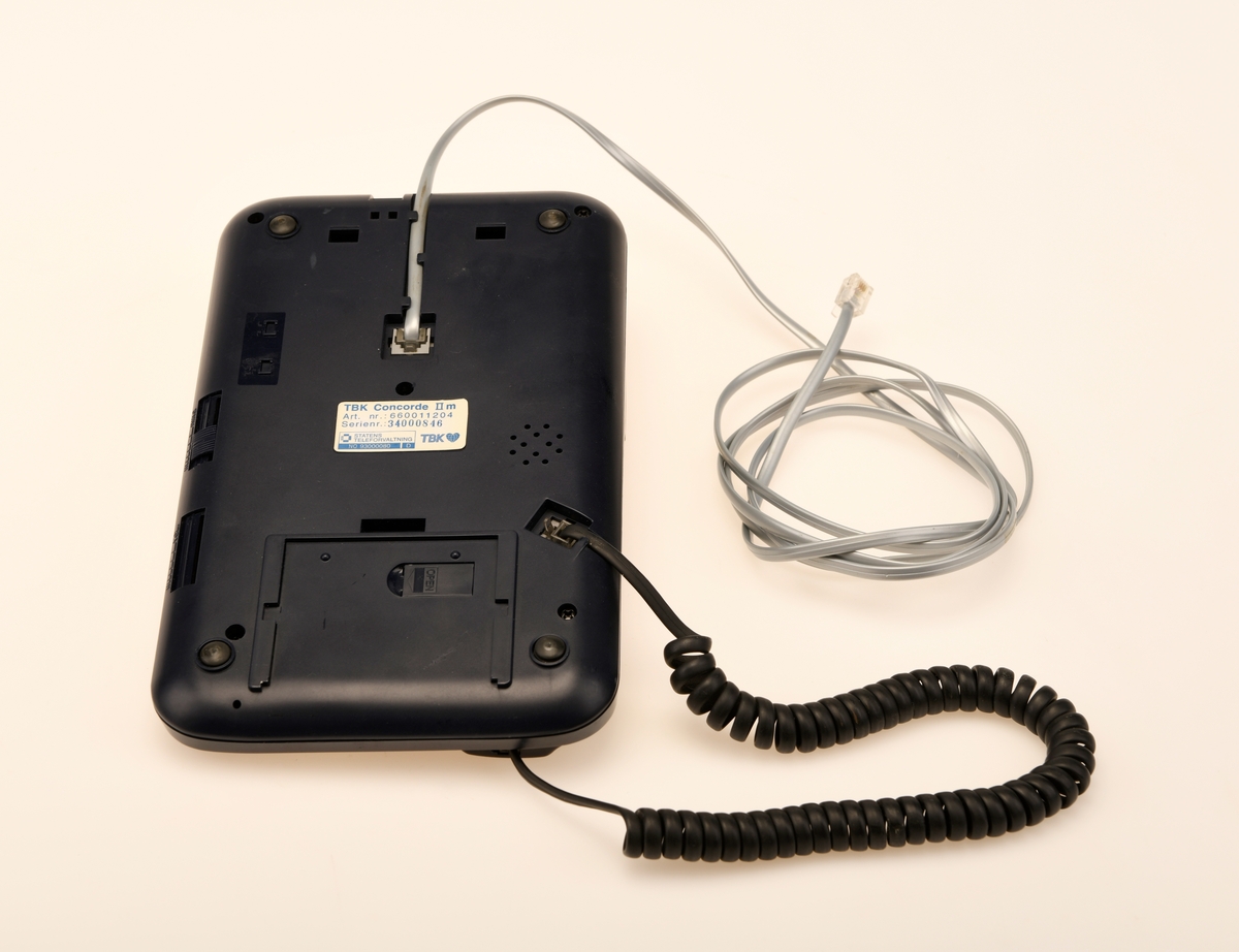 Sort bordtelefon med 23 taster fra TBK. Telefonen er av modelltypen TBK Concorde II m. Telefonen kommer med en svart spirallisert ledning til telefonrøret og en hurtigkopling i grått.
