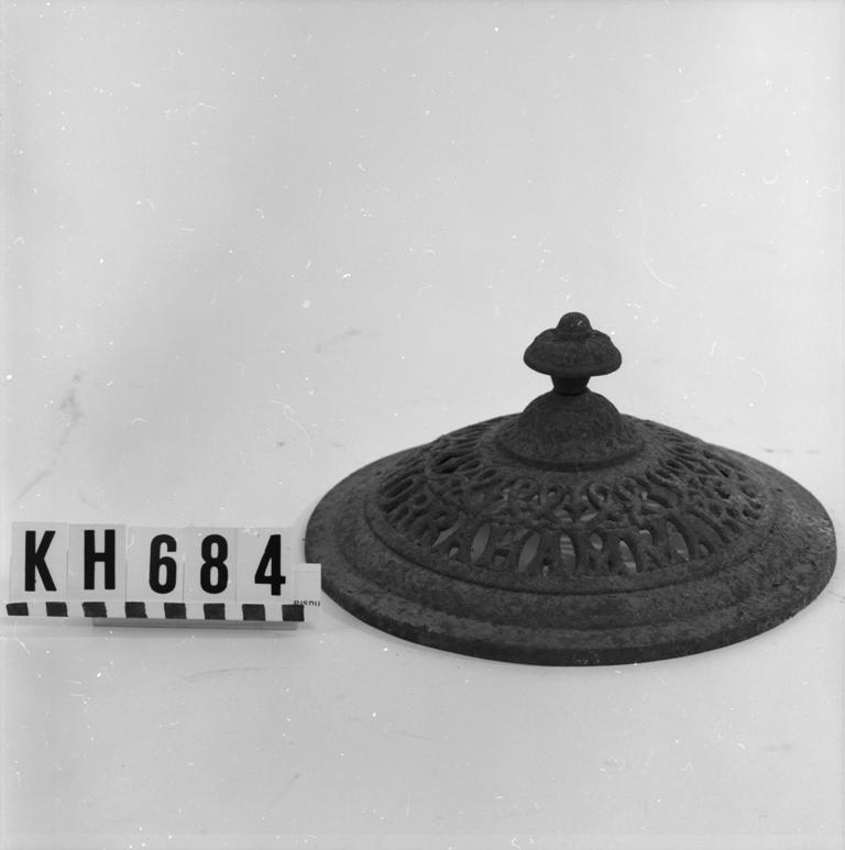 Utgå? Överdel/lock till kamin. Knoppen fastskruvad med bult genom godset. Gallerliknande mönster med texten "Norrahammar No.10".
Funktion: tillbehör till en oftast fristående ugn för rumsuppvärmning.