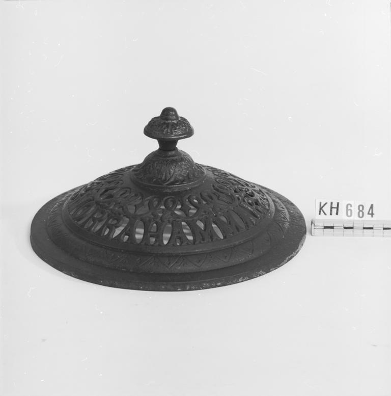 Utgå? Överdel/lock till kamin. Knoppen fastskruvad med bult genom godset. Gallerliknande mönster med texten "Norrahammar No.10".
Funktion: tillbehör till en oftast fristående ugn för rumsuppvärmning.