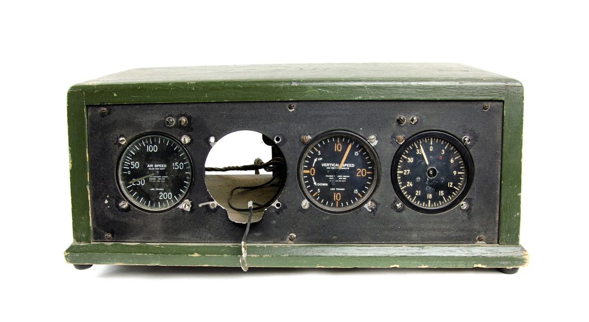 Linktrainer Instrumentpanel, till simulator. Rektangulär trälåda i grönt utförande, instrumentpanelen har fyra mätare varav en av dessa saknas. I utbildningssyfte.