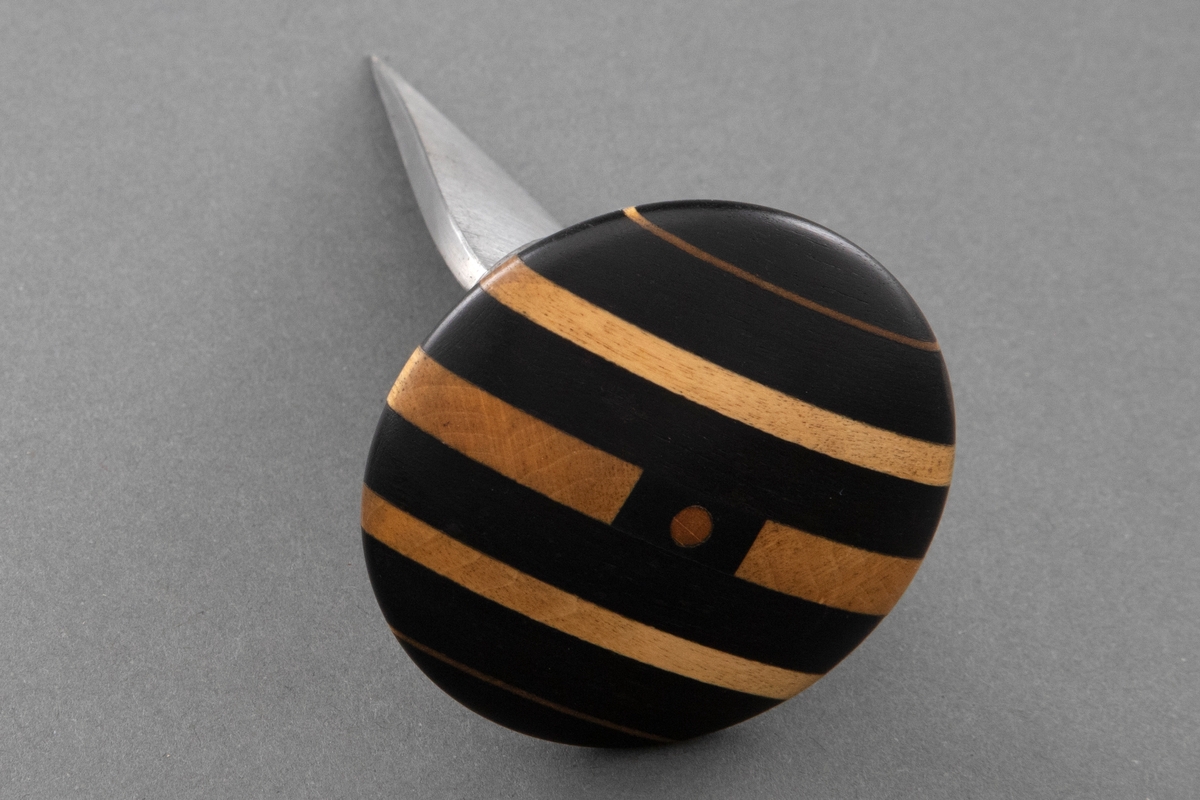 Kort blad av stål er festet til skaftet med en sølvholk. Soppformet skaft, laminert vekselsvis mørkt og lyst tre.