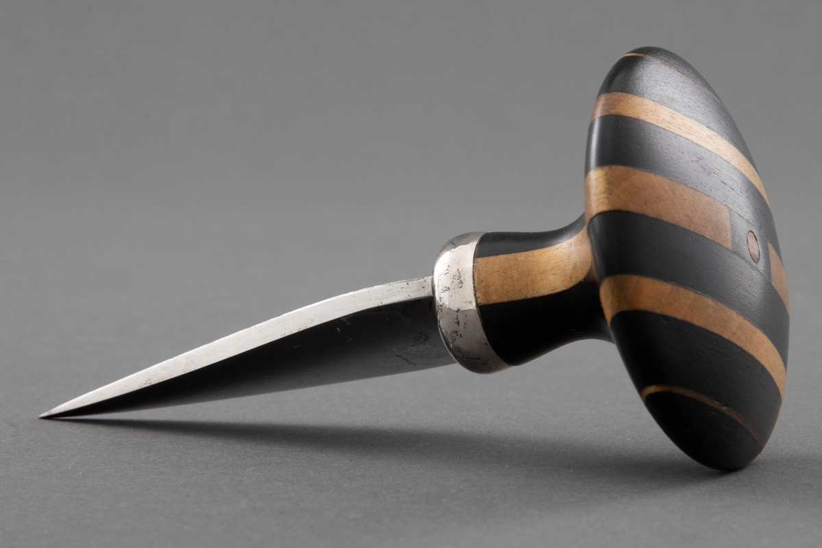 Kort blad av stål er festet til skaftet med en sølvholk. Soppformet skaft, laminert vekselsvis mørkt og lyst tre.