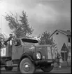 Realexamen 1961. Bilden föreställer ett lastbil, på flaket står flera studenter. De bär studentmössa och blombuketter runt sina halsar. Flaket är klätt med Björkris och ballonger. Två kvinnor sticker ut sina överkroppar genom fönstret på passagerarsidan på lastbilen.