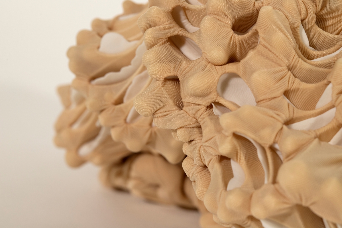 Objekt/ skulptur med organisk form. Beige nylon er knyttet og sydd rundt porselensskiver og foldet. Formen kan minne om et kadaver.