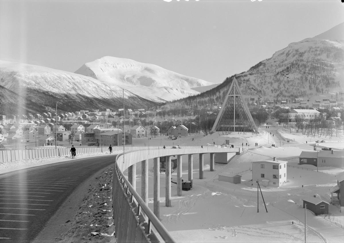 Arkitekturfoto av Tromsdalen kirke, bedre kjent som Ishavskatedralen. Med sitt avtrappede båthusformede eksteriør og sine åpne glassgavler er den blitt et landemerke i området. Kirken ble innviet 19. november 1965.