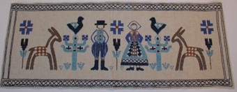 Mönstret inspirerat av vävnad från Toarp. Bearbetad av Margaretha Harström. Mönsterritning finns i mapp BM 75095+garnkarta. Broderiprov finns i mapp BM 75095. Kalkyl finns i särskild      pärm.

Broderad bonad. Dam och herre i folkdräktsliknande kläder i olika blå toner. Stiliserade träd vid sidorna med fågel på toppen. Bockar i profil längst ut på kanterna. Rutmönstrad blå bård i        stjälkstygn.
