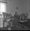 Realskolebilder Nyarp 1961. En kvinna sitter omgiven av krukväxter och blombuketter.