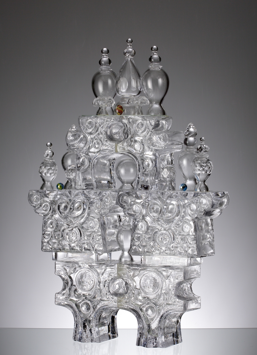 Glasskulptur. "Kristallslott".
Stiliserat slott med tinnar och torn i tre etage.
Formblåst, hyttarbetat, friblåst, slipat.
Översta plattformens spiror är monterade på en glasplatta som är spräckt. (Detta påverkar inte konstruktionen eller utseendet. 2010-01-21) .
Klarglas.

Föremålet har varit i L. Hellstens ägo i Nybro fram till 2009.

Övrigt: Kristallslottet är bland de första L.H. gjorde på Skrufs glasbruk.Han inspirerades av hyttmiljön, som han tyckte var som ett sagolandskap. Det finns tre slott, ett på Smålands Museum, ett på Nationalmuseum och ett på Röhsska Museet.
Funktion: Glasskulptur