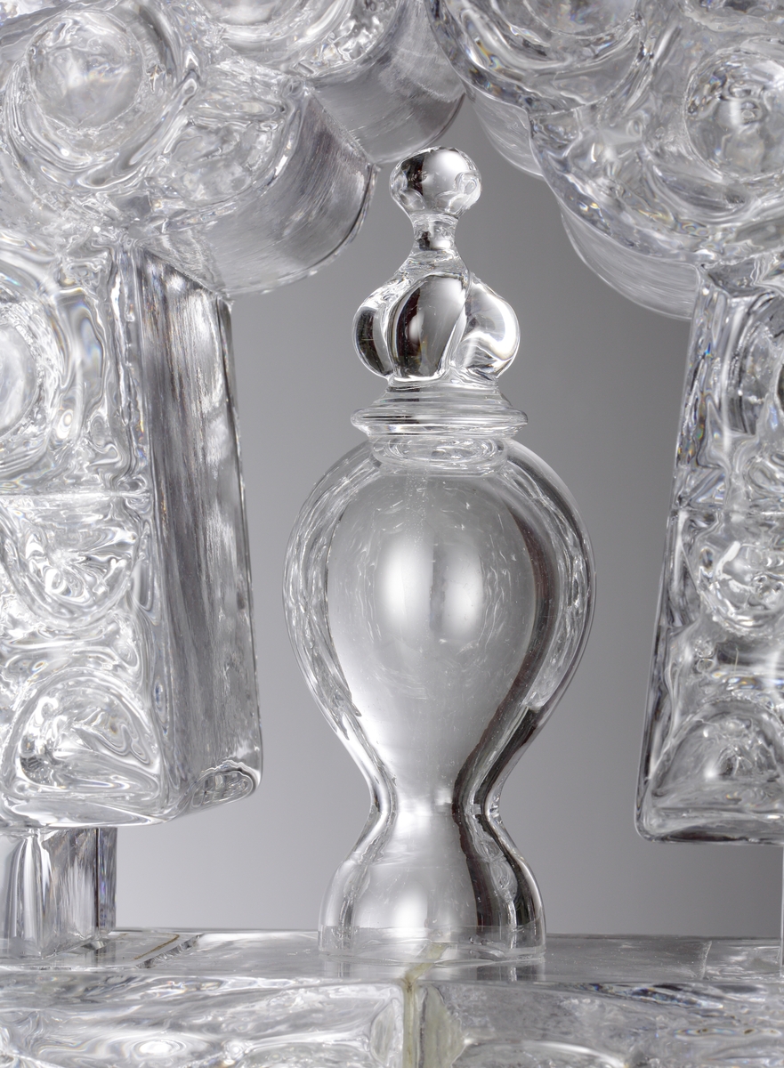 Glasskulptur. "Kristallslott".
Stiliserat slott med tinnar och torn i tre etage.
Formblåst, hyttarbetat, friblåst, slipat.
Översta plattformens spiror är monterade på en glasplatta som är spräckt. (Detta påverkar inte konstruktionen eller utseendet. 2010-01-21) .
Klarglas.

Föremålet har varit i L. Hellstens ägo i Nybro fram till 2009.

Övrigt: Kristallslottet är bland de första L.H. gjorde på Skrufs glasbruk.Han inspirerades av hyttmiljön, som han tyckte var som ett sagolandskap. Det finns tre slott, ett på Smålands Museum, ett på Nationalmuseum och ett på Röhsska Museet.
Funktion: Glasskulptur