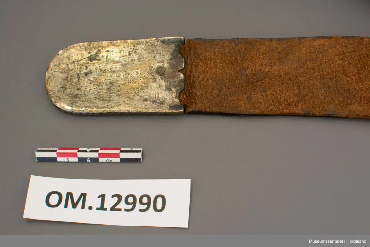 Stølabelte og fangreim i eitt. Eit langt lærstykke der det i eine halvdelen er montert 19 firkanta stølar, og i den andre enden 6 runde, små, blomsterliknande borer. Dei ulike delane har festeringar som går gjennom hol i leret, og vert festa på baksida ved at ei snor av bomull vert trekt gjennom ringane. Endestykke nedst på fangreima. På baksida er nokre svake merker: Nokre X-ar og ein L. Beltet har mykje restar av pussemiddel.