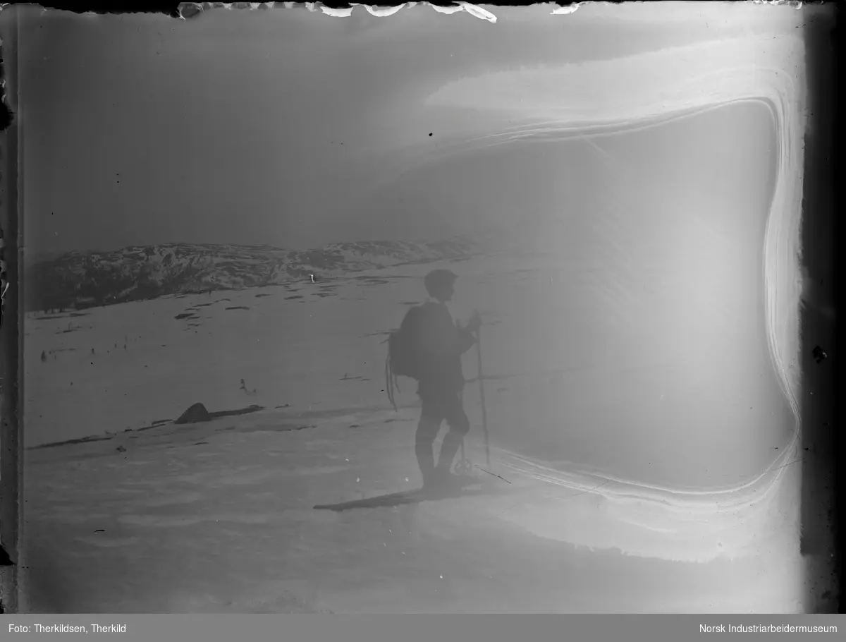 Mann på skitur på fjellvidde. Mannen er kledd i knickers, sixpence og sekk på ryggen.