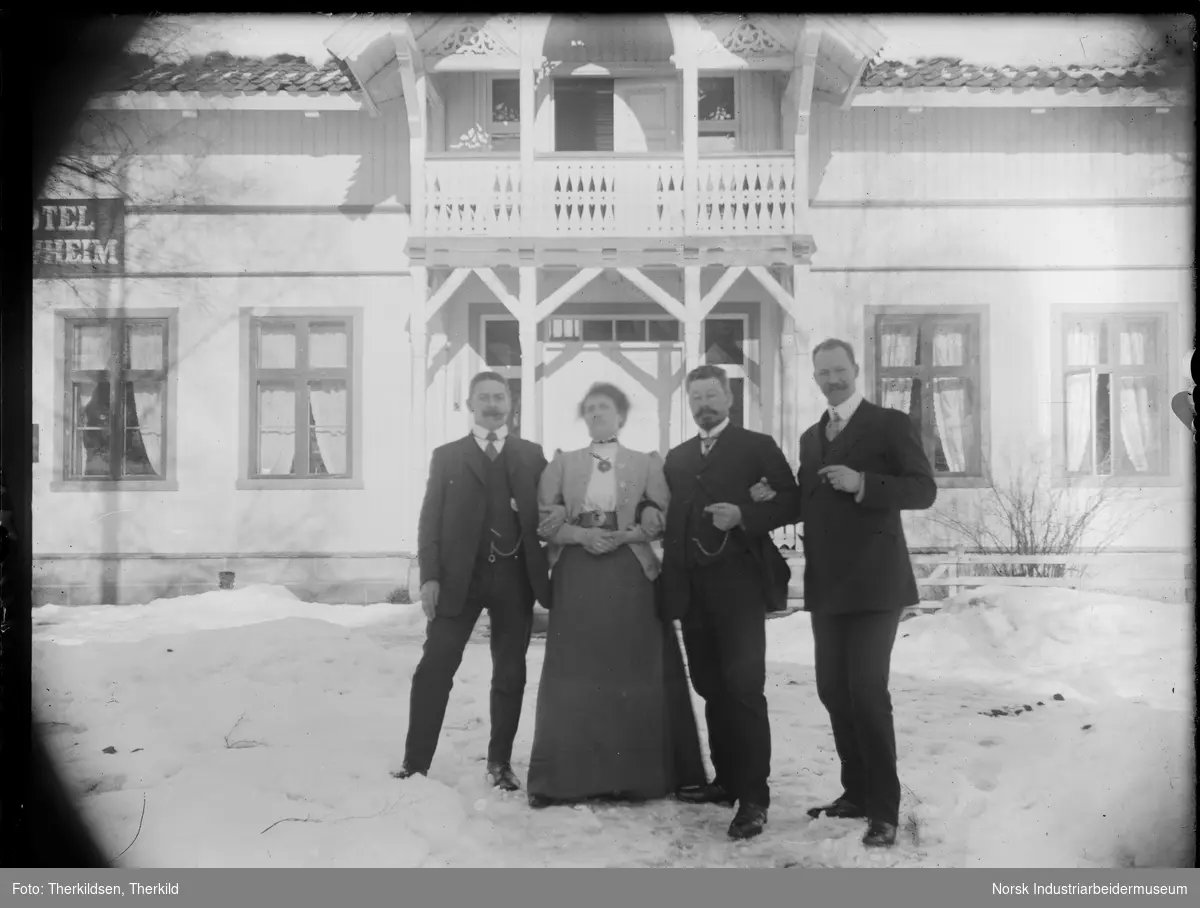 En kvinne og tre menn stående utenfor Løvheim hotell. Alle holder hverandre i armene.