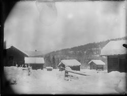 Gårdstun på Lien med fem bygninger vinterstid. Stige står le