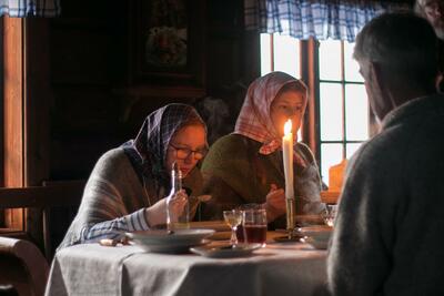 Julefeiring i Vestaberg. To jenter med skaut, og kledd anno 1900, spiser julemiddag.