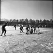 Realskolans vinterlov januari 1961. Några unga personer spelar hockey. De är action runt målet. En person bär hjälm resten bär mössor på huvudet.