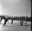 Realskolans vinterlov januari 1961. Några unga personer spelar hockey. Målvakten har precis räddat en puck från att gå in i mål. Pucken flyger strax över fötterna på målvakten. En person bär hjälm resten bär mössor på huvudet.