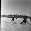 Realskolas vinterlov januari 1961. Några unga människor spelar hockey på en istäckt sjö. En bär benskydd och klubba. De är i rörelse så bilden är oskarp.