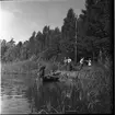 Rotenonbehandling i Bergadammen 1961. Fyra män står på en kaj intill en sjö. Två män befinner sig i en roddbåt på sjön, en man sitter vid årorna och en man står med ett långt munstycke som leder till en metallbehållare.