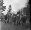 Skolungdomar på Grännaberget 1961. Ungdomarna bär mössa eller sjalett. I mitten står en äldre herre och talar.