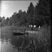 Rotenonbehandling i Bergadammen 1961. Fyra män står på en kaj intill en sjö. Två män befinner sig i en roddbåt på sjön, en man sitter vid årorna och en man står med ett långt munstycke som leder till en metallbehållare.