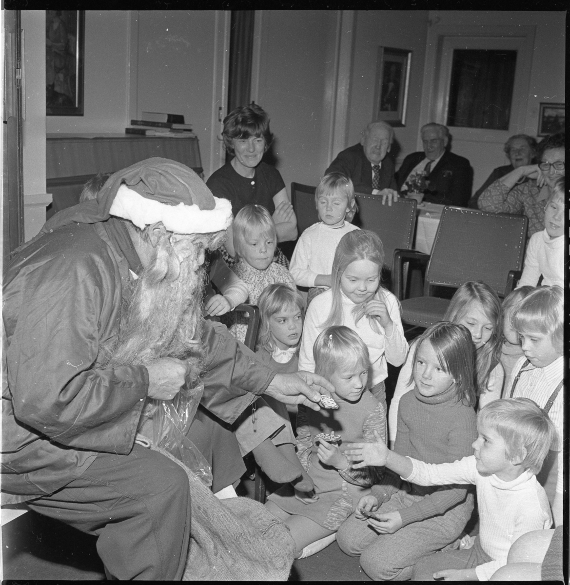 En jultomte sitter på en stol framför barn.